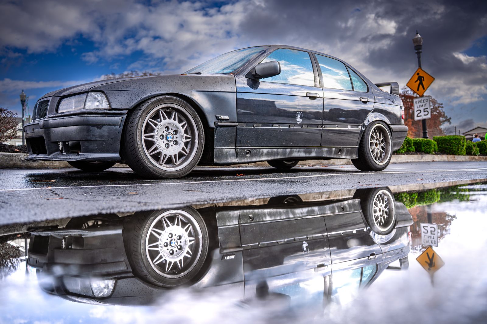BMW Serie 3 oscuro reflejado en un charco bajo un cielo nublado