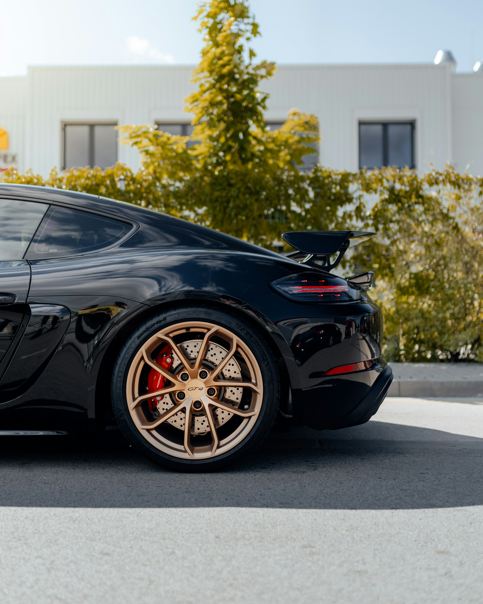 Rear quarter of a black Porsche Cayman GT4 with a bronze wheel