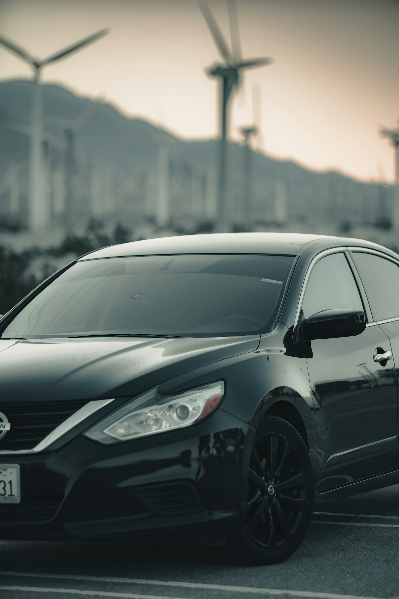 Black Nissan Altima parked with wind turbines in the background