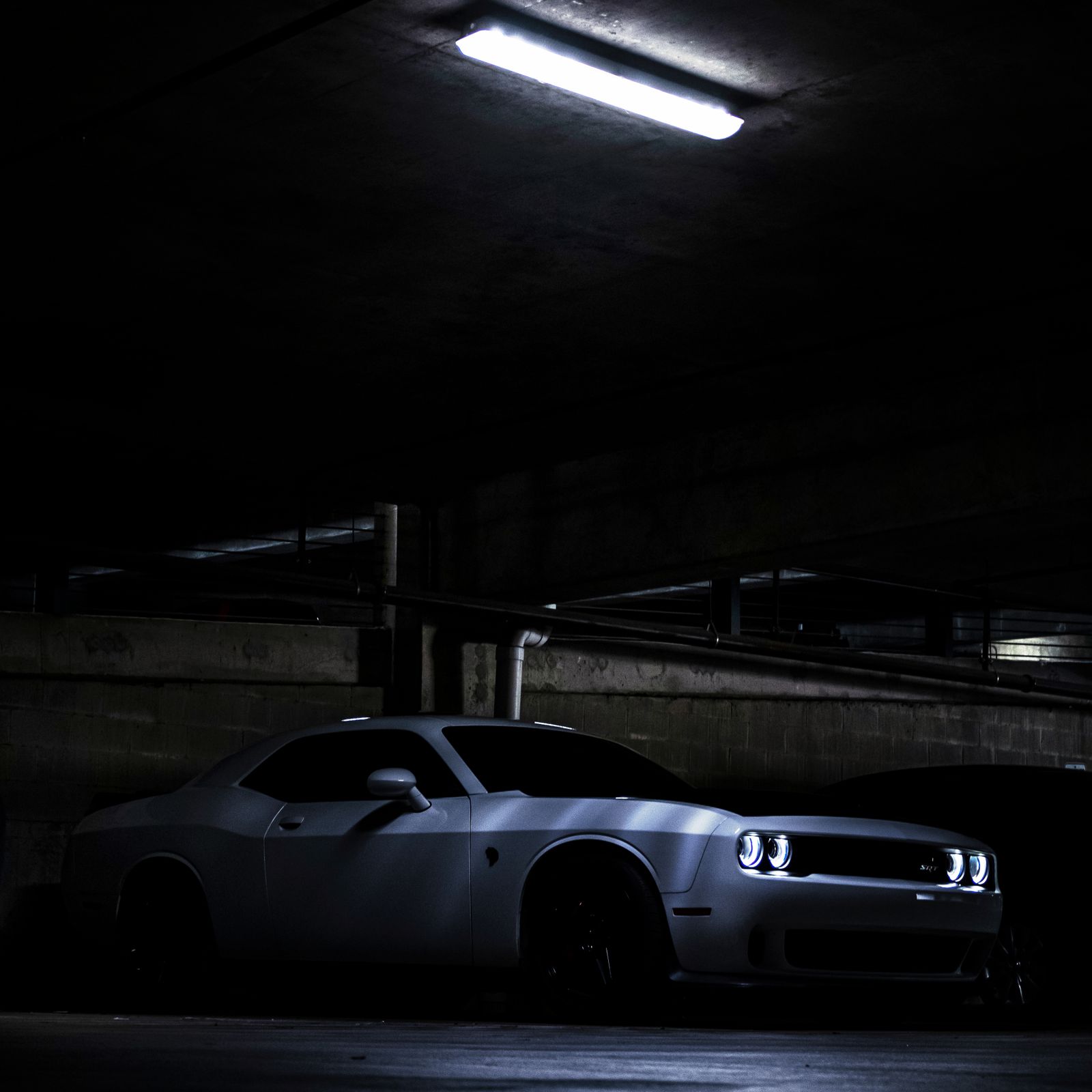 Dodge Challenger Hellcat blanco aparcado en un garaje poco iluminado con los faros encendidos